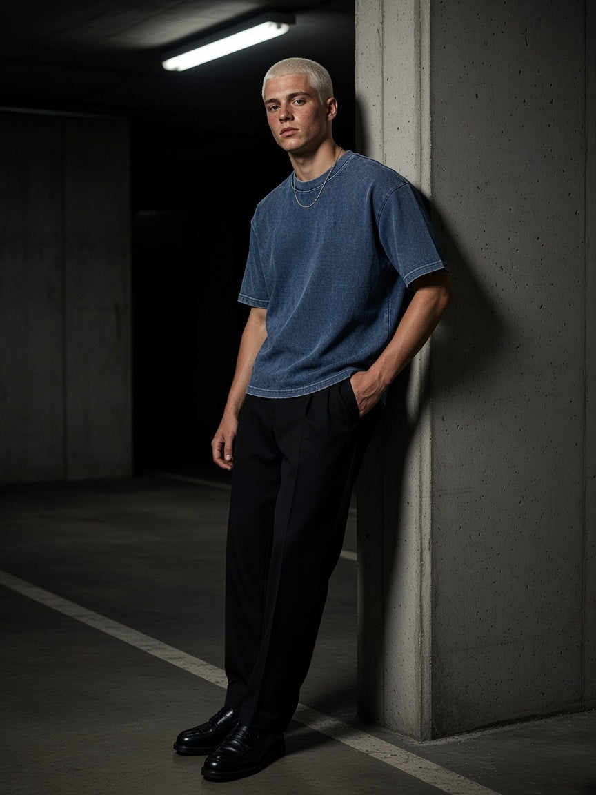 Man in the Textured Waffle Washed Boxy T-Shirt in Haze Blue leaning on a pillar in a Berlin car park at night
