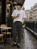 Man in the Loose Fit Tapered Joggers in Dark Gray with a coffee on a Paris cafe terrace on a grey morning