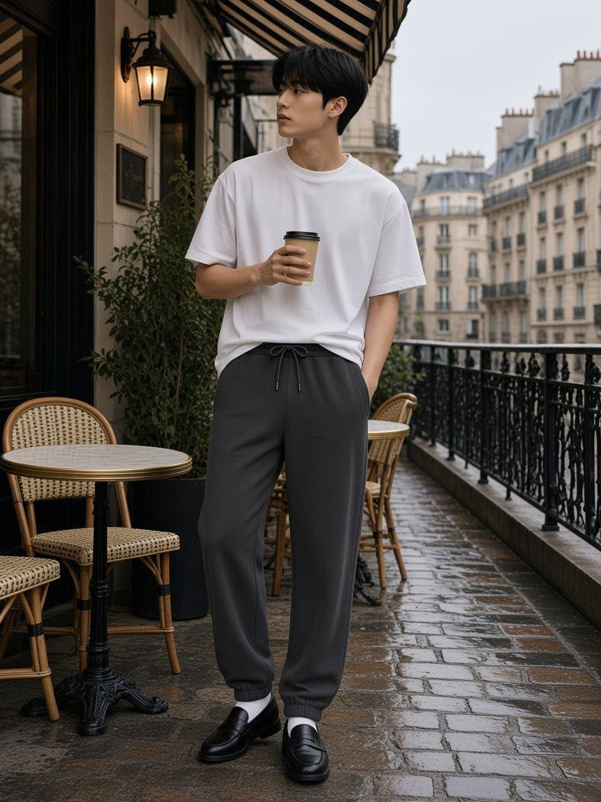Man in the Loose Fit Tapered Joggers in Dark Gray with a coffee on a Paris cafe terrace on a grey morning
