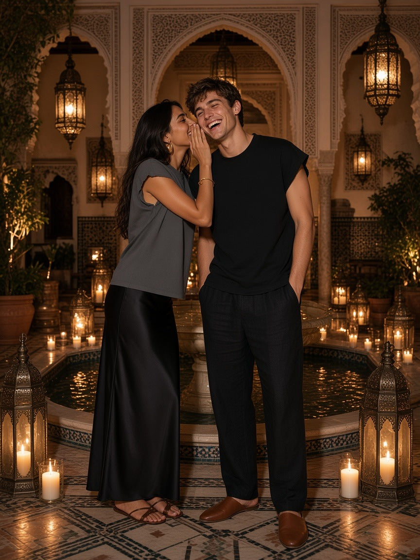 Marcel Afters Boxy Raw Edge T-Shirt in Black, worn by a man and a woman, whispering in a candle-lit courtyard fountain room, she in grey and he in black boxy tees