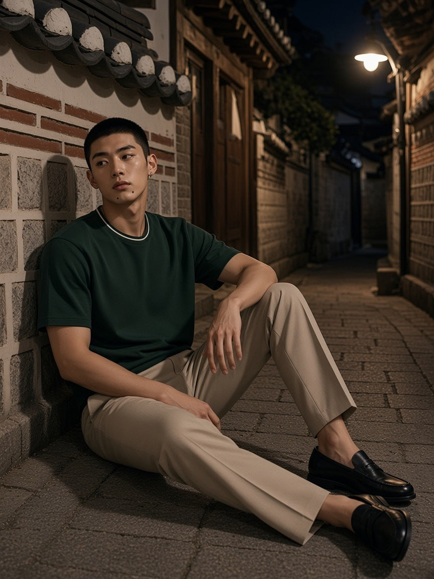 Man in the Boxy Ribbed T-Shirt in Dark Green seated against a hanok wall in Bukchon, Seoul at night