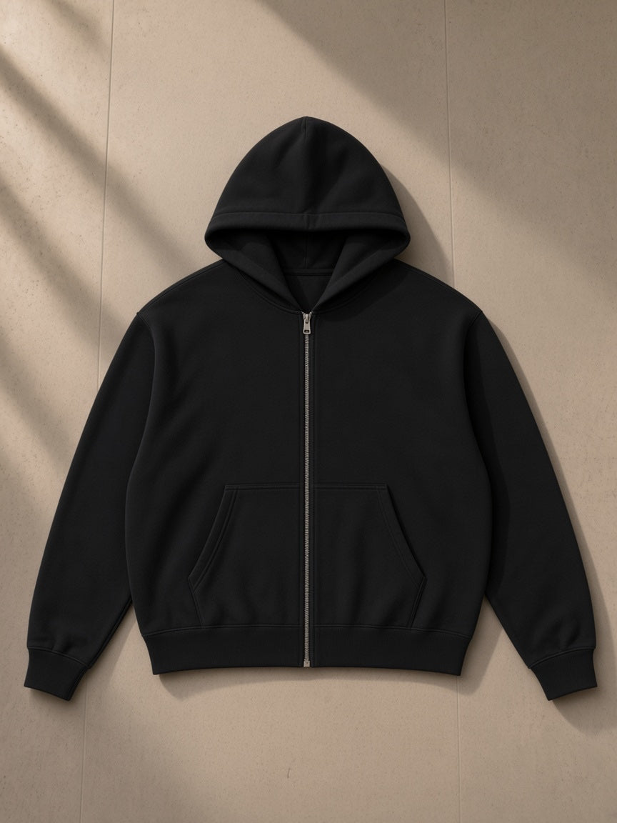 Unisex drop-shoulder zip up hoodie in Black, laid flat on pale limestone, front view