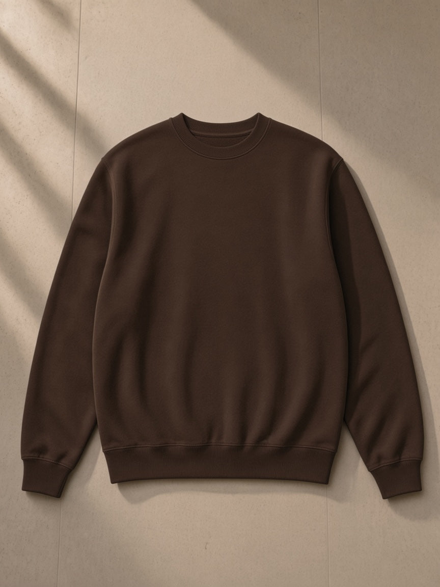 Unisex heavyweight crewneck sweatshirt in Coffee, laid flat on pale limestone, front view