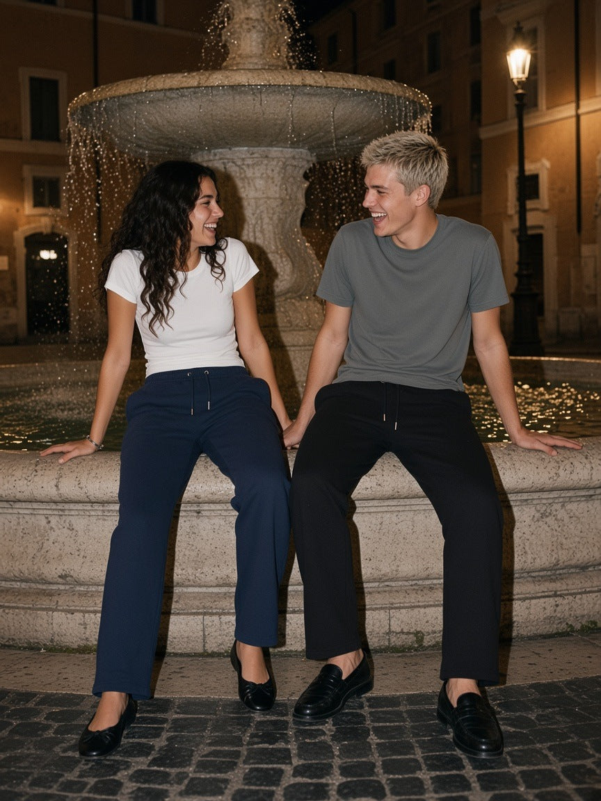Marcel Afters Heavyweight Sweatpants in Navy Blue, worn by a man and a woman, seated on a fountain edge at night, she in navy sweatpants and he in black