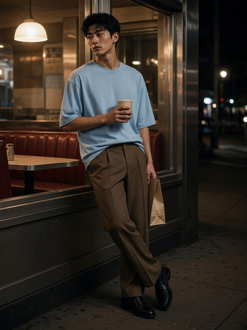 Man in the Lightweight Oversized T-Shirt in Haze Blue with a coffee outside a Bowery diner in New York at night