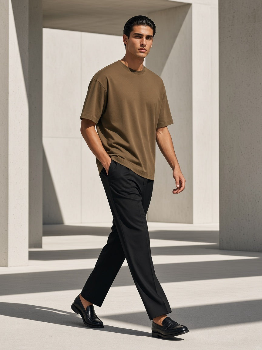 Man in the Marcel Afters Oversized Drop Shoulder T-Shirt in Brown, walking through a sunlit concrete colonnade