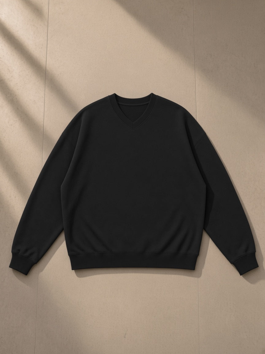 Unisex oversized v-neck sweatshirt in Black, laid flat on pale limestone, front view