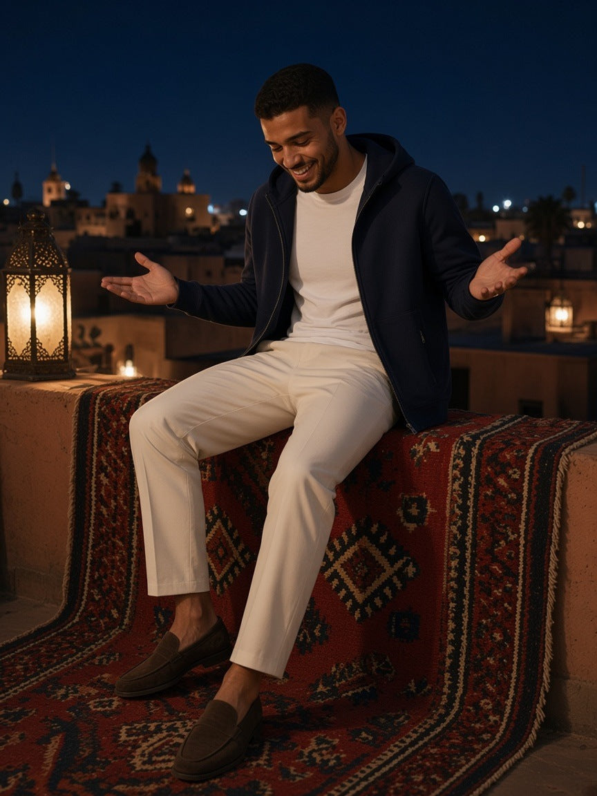 Man in the Paneled Full-Zip Hoodie in Navy Blue over a white tee with ecru trousers and suede loafers, laughing on a Marrakech rooftop at night