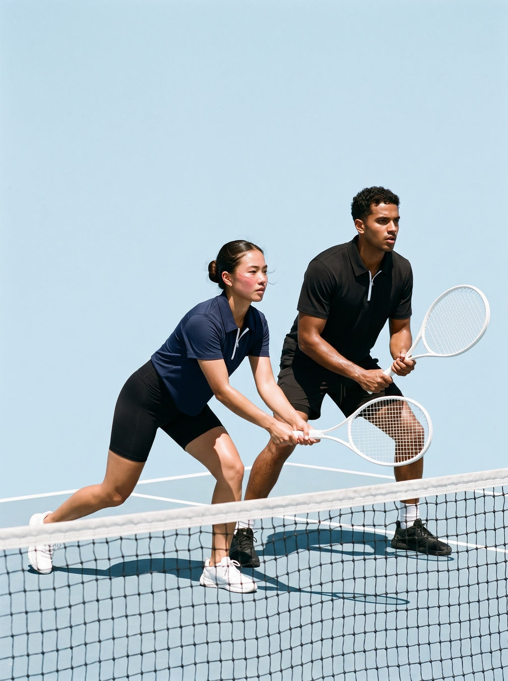 Two people in the Quarter-Zip Polo Shirt, a man in Black and a woman in Navy Blue, playing doubles at the net on a hard tennis court