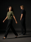 Two people in the Seamless Cotton T-Shirt in Army Green and Black, a woman walking in heels, a man looking back, charcoal studio
