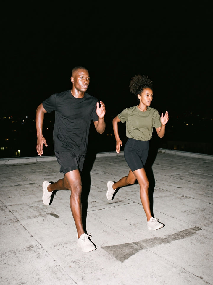 Two people in the Sorona Quick-Dry T-Shirt, a man in Black and a woman in Olive Green, running across a rooftop at night
