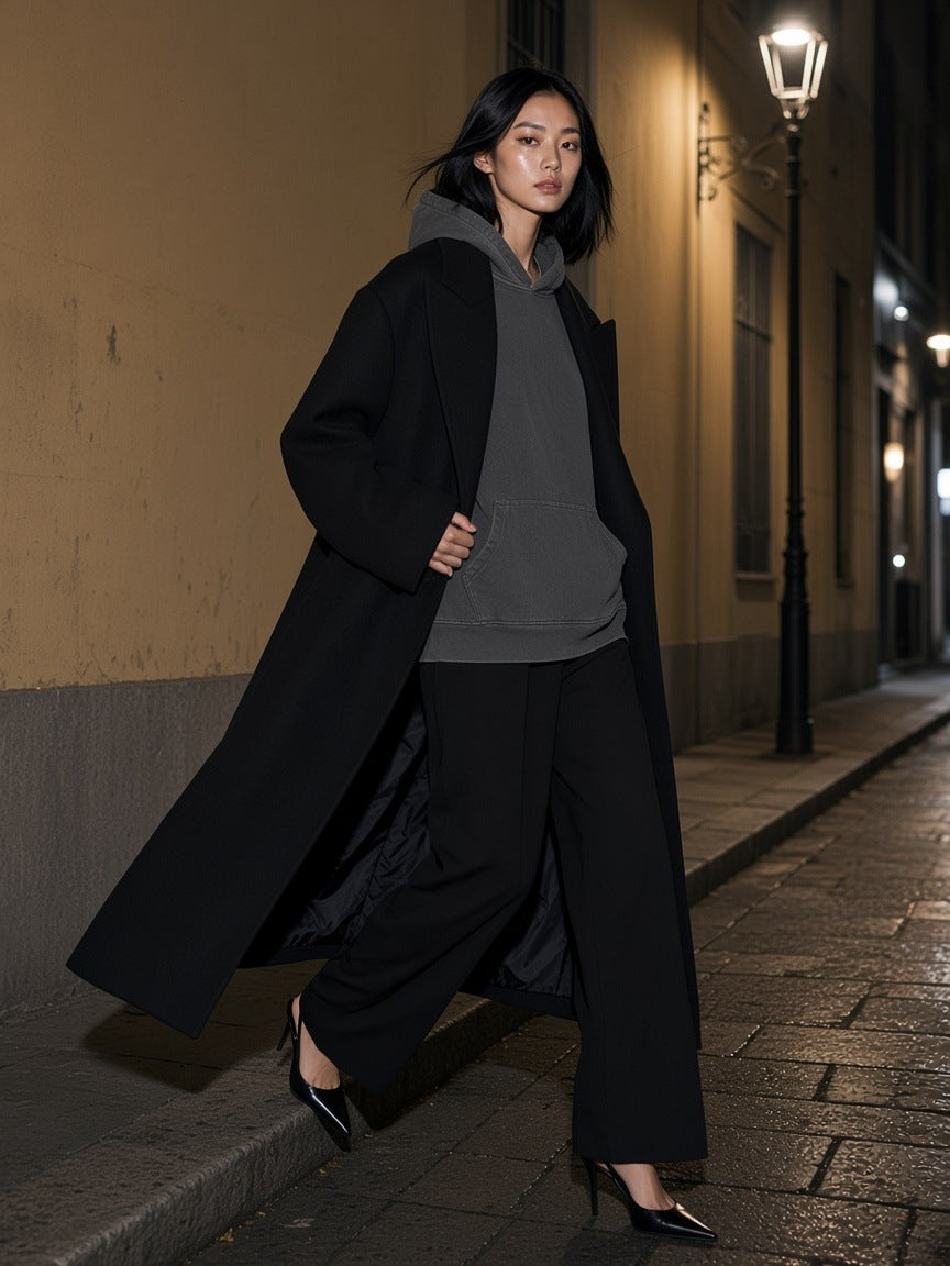 Woman in the vintage wash boxy hoodie in Dark Gray under a long black coat, stepping off a kerb on a Brera side street in Milan at night