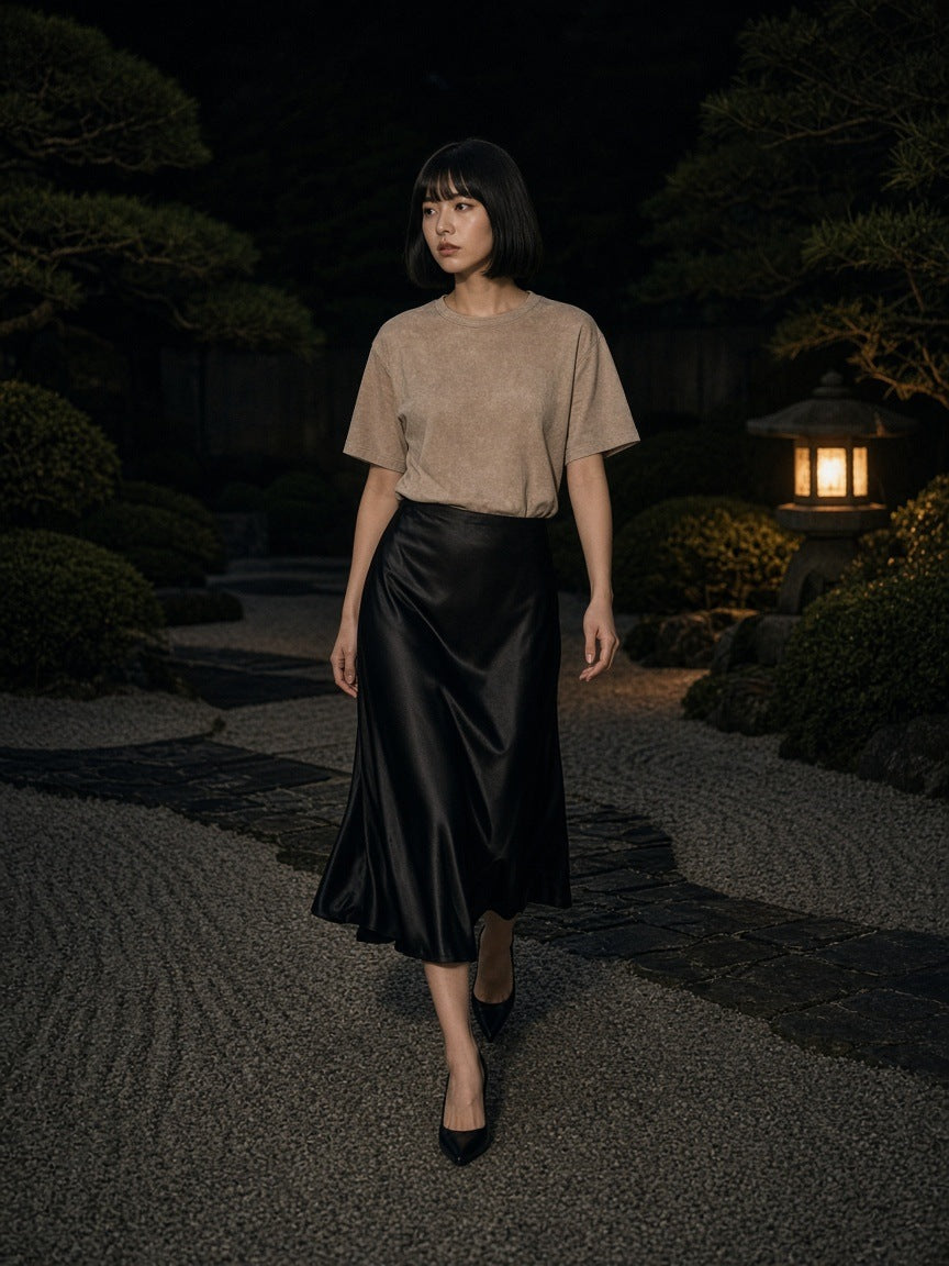 Woman in the Vintage Wash Boxy T-Shirt in Light Coffee with a black satin skirt in a stone garden at a hotel in Tokyo at night