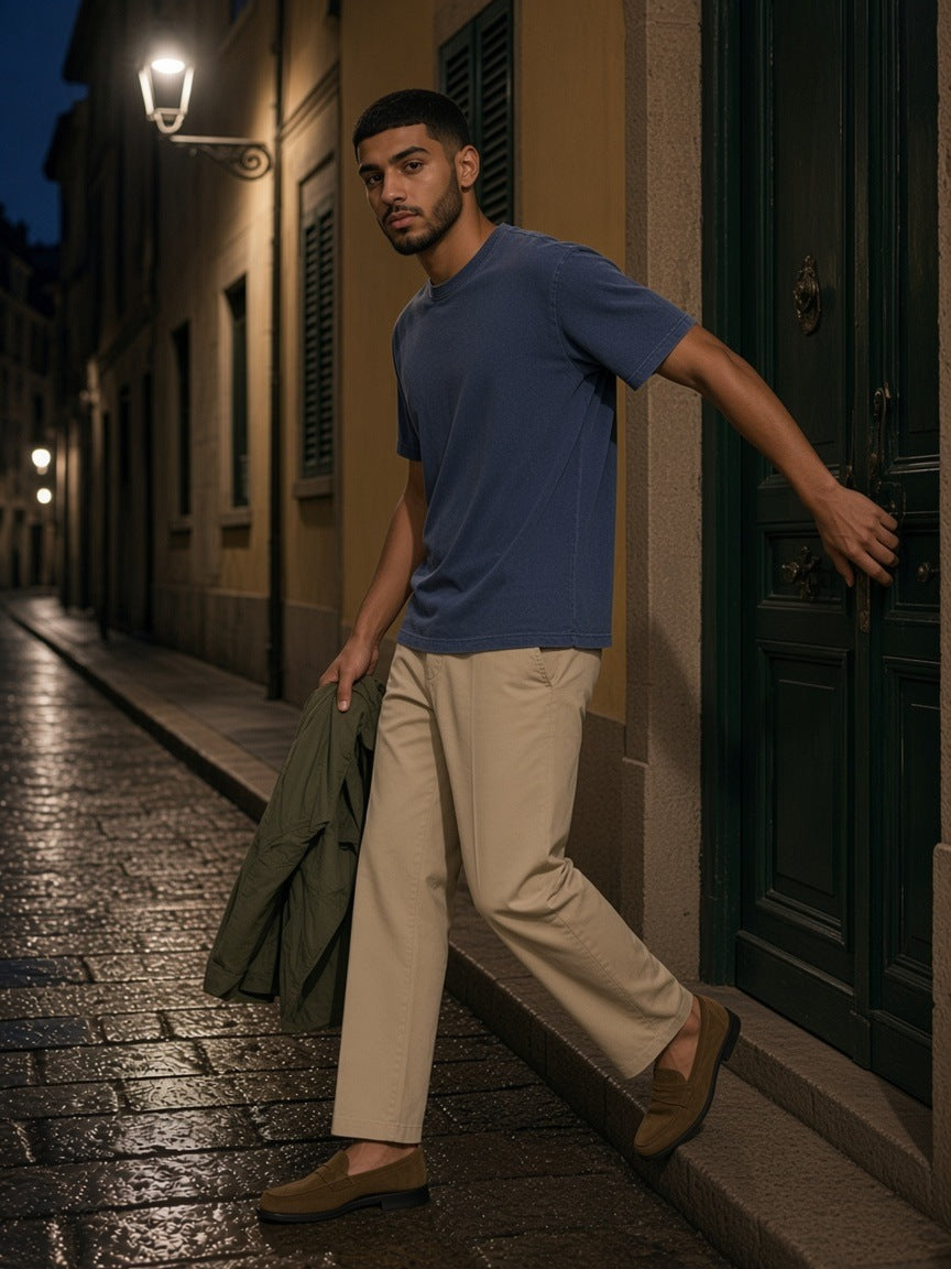 Man in an indigo vintage wash boxy t-shirt and khaki chinos pushing open a green door on a lamplit street