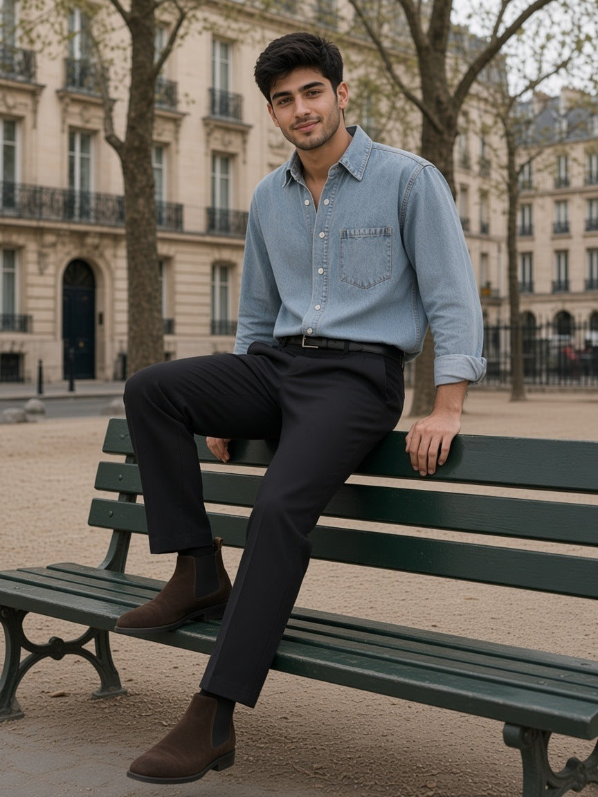 Man in a light vintage wash denim shirt and black trousers sitting on a Paris park bench