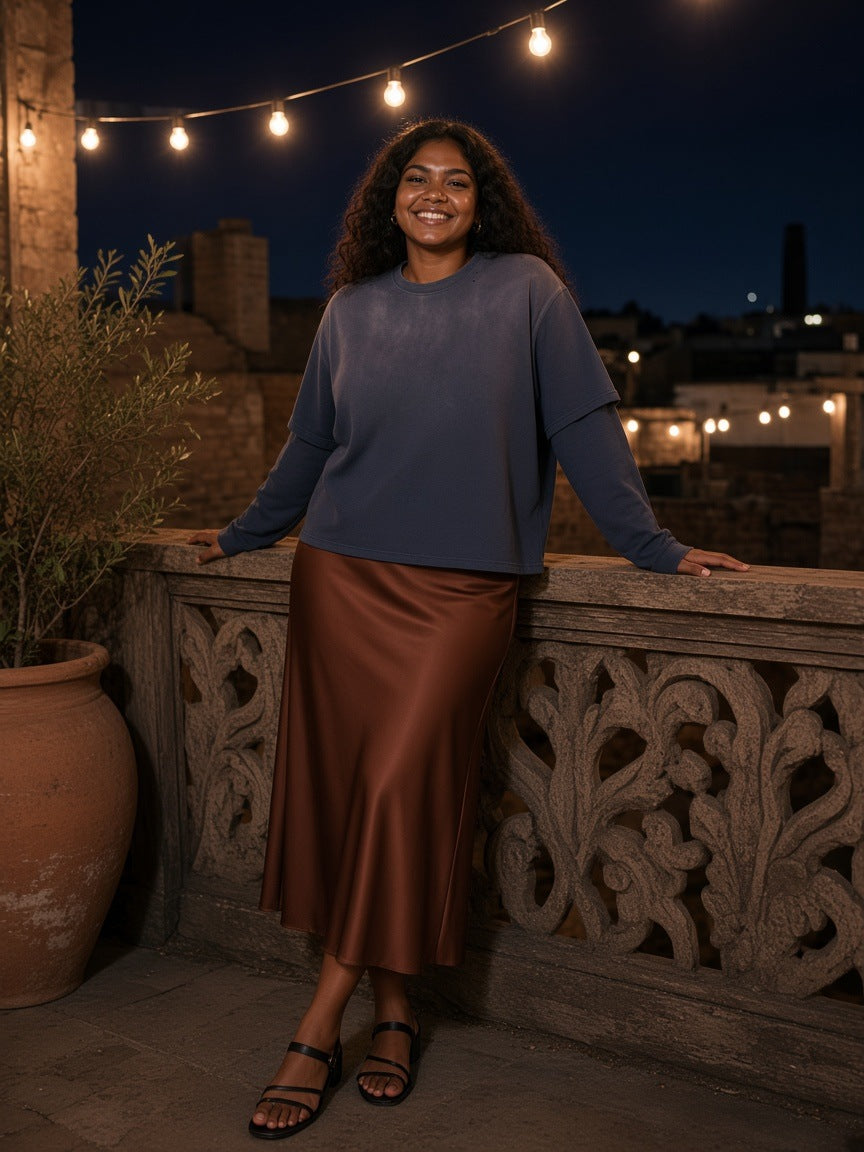 Woman in the Vintage Wash Layered T-Shirt in Navy Blue with a rust satin midi skirt and strappy sandals, on a Tbilisi rooftop terrace at night