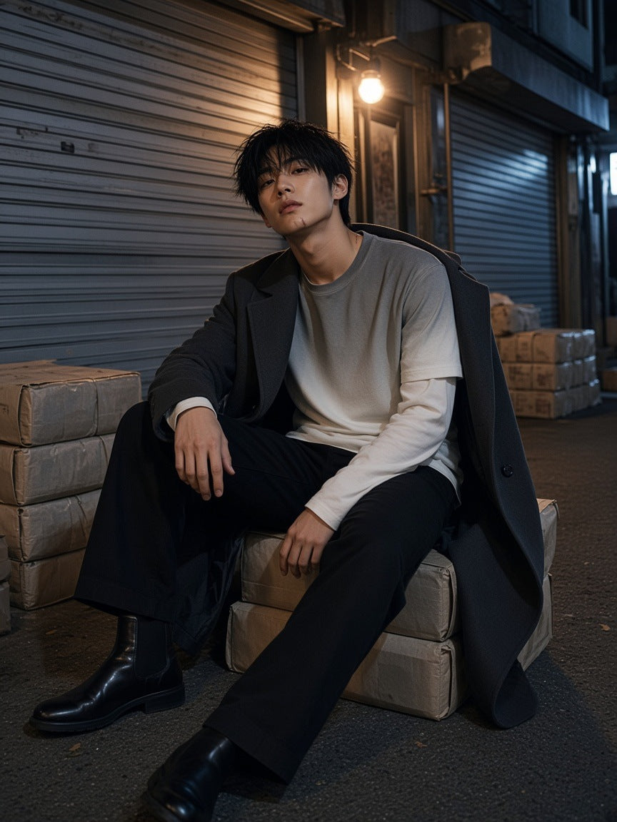 Man in the Vintage Wash Layered T-Shirt in White Gray with black trousers and Chelsea boots, sitting on paper bales in a Seoul print lane at night