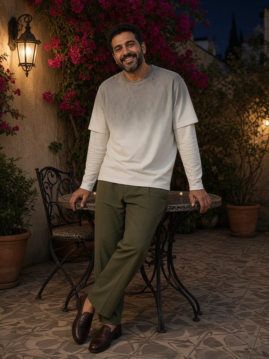 Man in the Vintage Wash Layered T-Shirt in White Gray with olive pleated trousers and brown loafers, in a bougainvillea courtyard in Mexico City at night