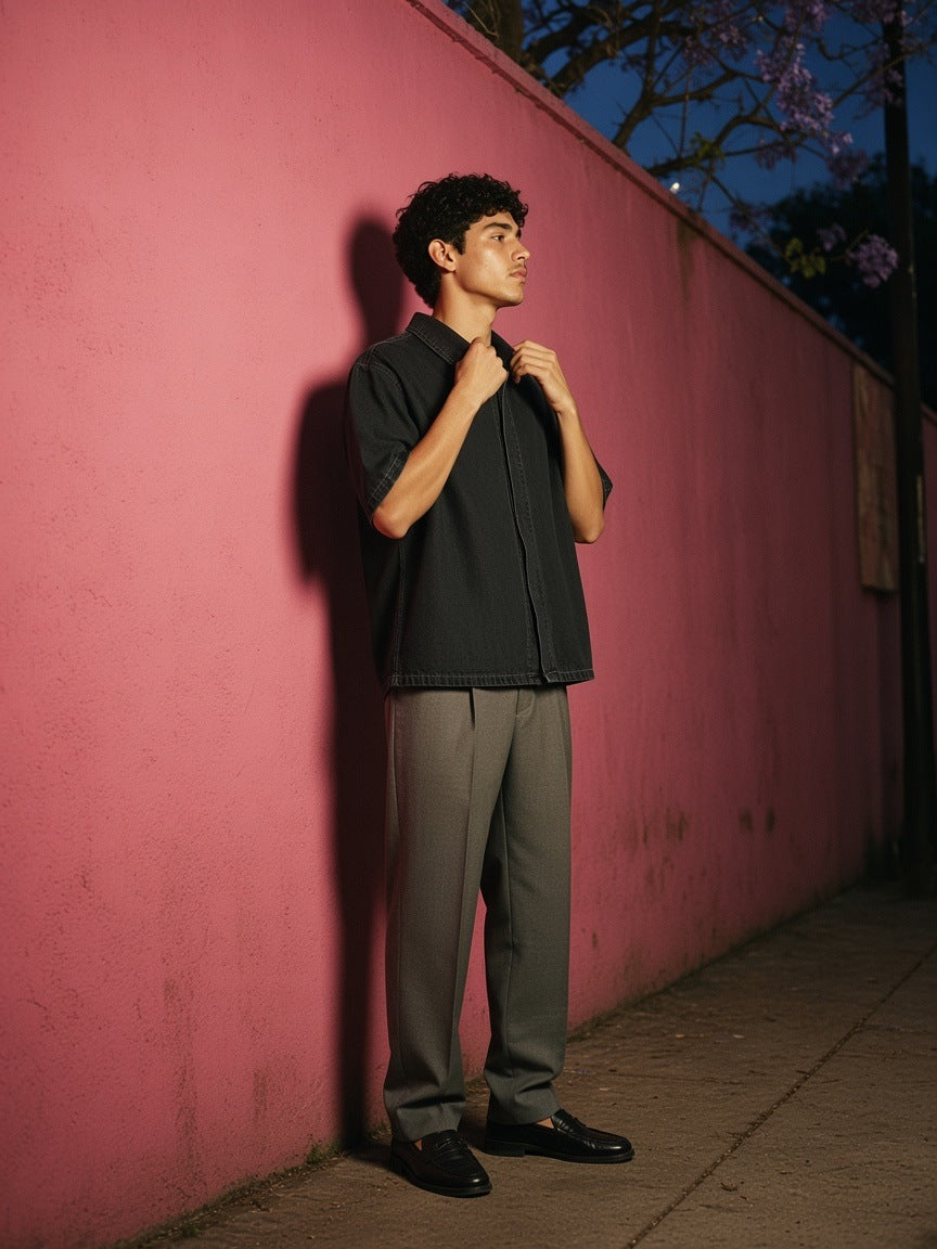 Man in the Vintage Wash Lyocell Shirt in Black, straightening his collar against a pink plaster wall in Mexico City at night