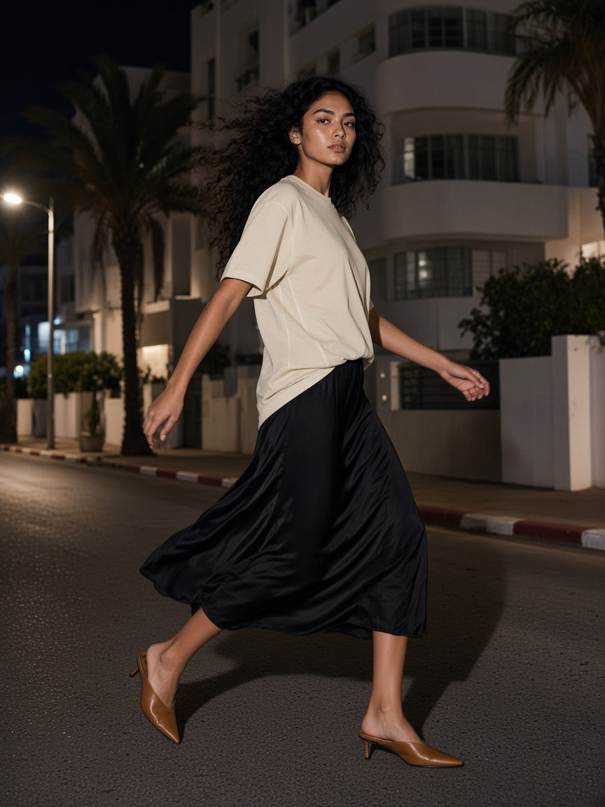 Woman in the Vintage Wash Paneling T-Shirt in Apricot on a white Bauhaus balcony in Tel Aviv at night