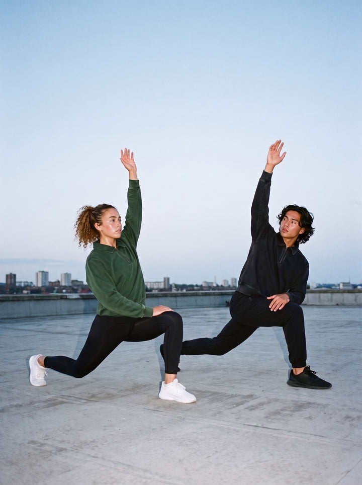 Two people in the Vintage Wash Quarter-Zip Sweatshirt, a man in Black and a woman in Blackish Green, stretching in deep lunges on a rooftop before sunrise