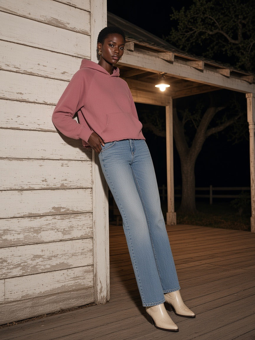Woman in the Marcel Afters vintage wash raw edge boxy hoodie in Carmine leaning on a dance hall porch in the Texas Hill Country at night