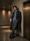 Man in the Vintage Wash Waffle Boxy Hoodie in Jeans Blue under a charcoal overcoat in a brutalist lift lobby at night