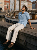 Man in the Vintage Wash Waffle Boxy Polo Shirt in Sky Blue seated on a harbour quay in Copenhagen in the morning