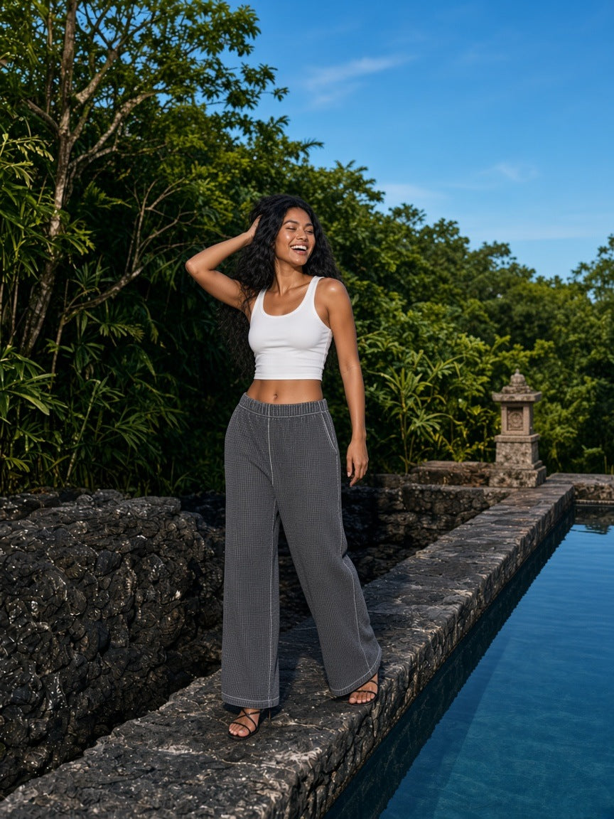 Woman in the Vintage Wash Wide Leg Mesh Sweatpants in Dark Gray walking a volcanic stone pool edge at a resort in Bali by day
