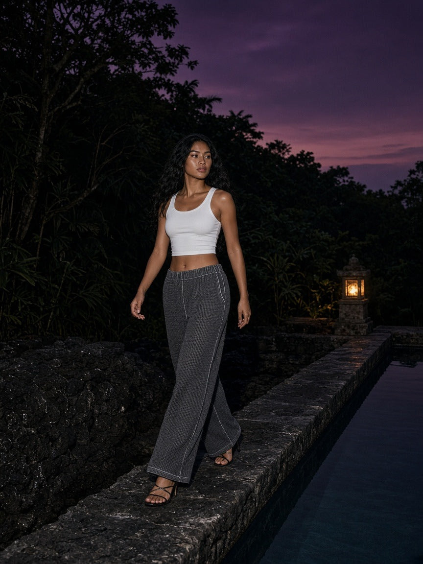 Woman in the Vintage Wash Wide Leg Mesh Sweatpants in Dark Gray walking a volcanic stone pool edge at a resort in Bali at dusk