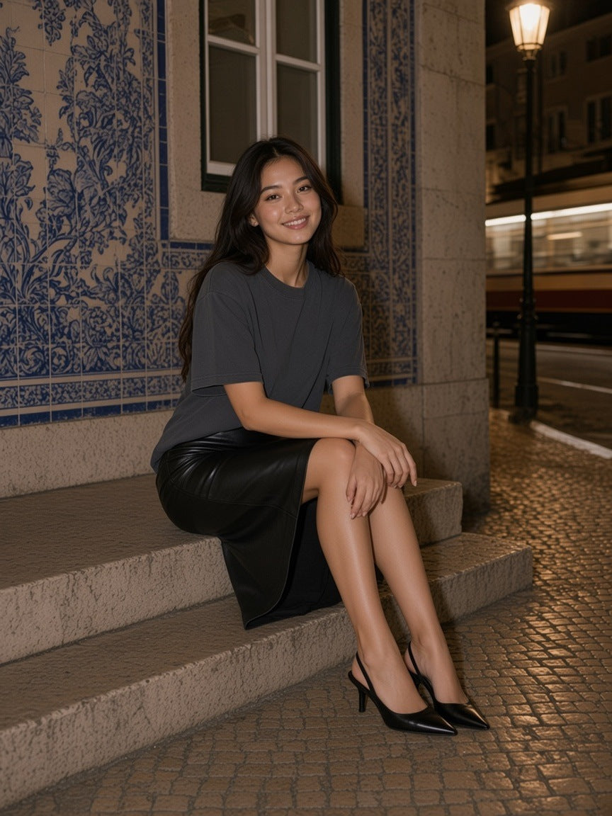 Woman in a Dark Gray vintage washed distressed boxy t-shirt and black leather skirt on a step by an azulejo wall at night