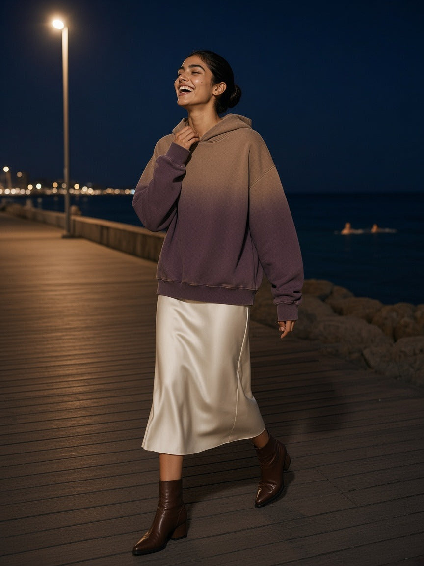 Woman in the vintage washed gradient fleece hoodie in Brown with an ivory satin midi skirt, laughing on the Barceloneta boardwalk in Barcelona at night