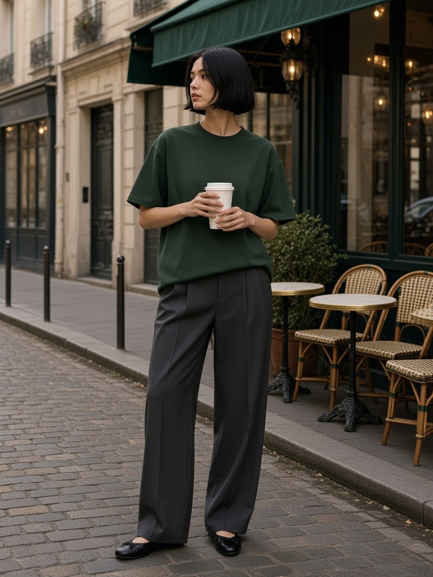 Woman in the Women's Heavyweight Earth Tone T-Shirt in Blackish Green with a coffee cup outside a Paris café terrace
