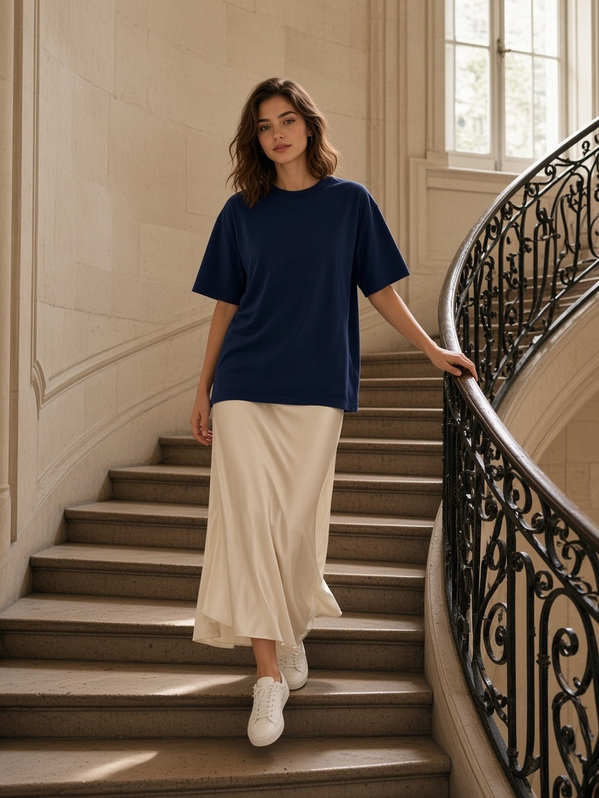Woman in the Women's Heavyweight Earth Tone T-Shirt in Navy and a cream satin skirt, coming down a curved stone staircase with a wrought-iron banister