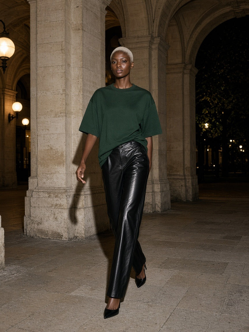 Woman in the Marcel Afters Women's Boxy Oversized T-Shirt — Dark in Dark Green walking a stone colonnade in Paris at night
