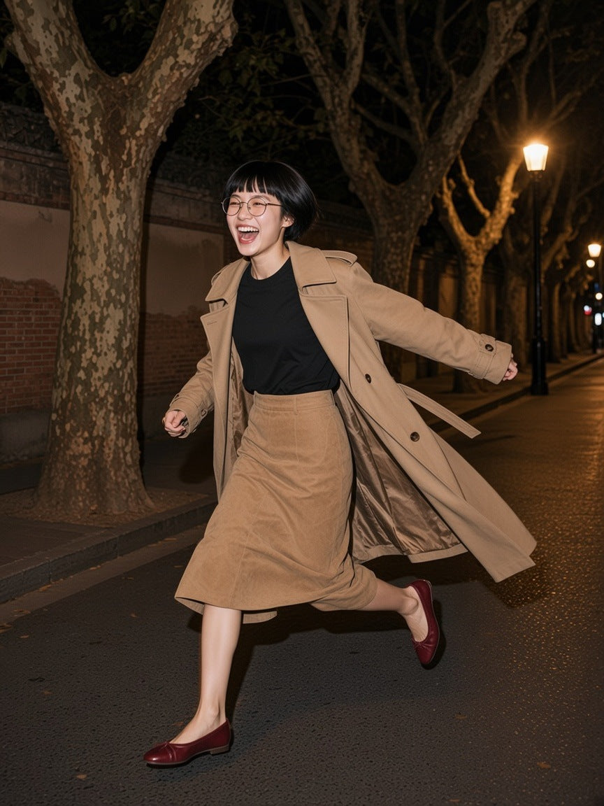 Woman in the Women's Essential Heavyweight Cotton T-Shirt in Black with a camel coat and skirt, running laughing down a plane-tree street in Shanghai at night