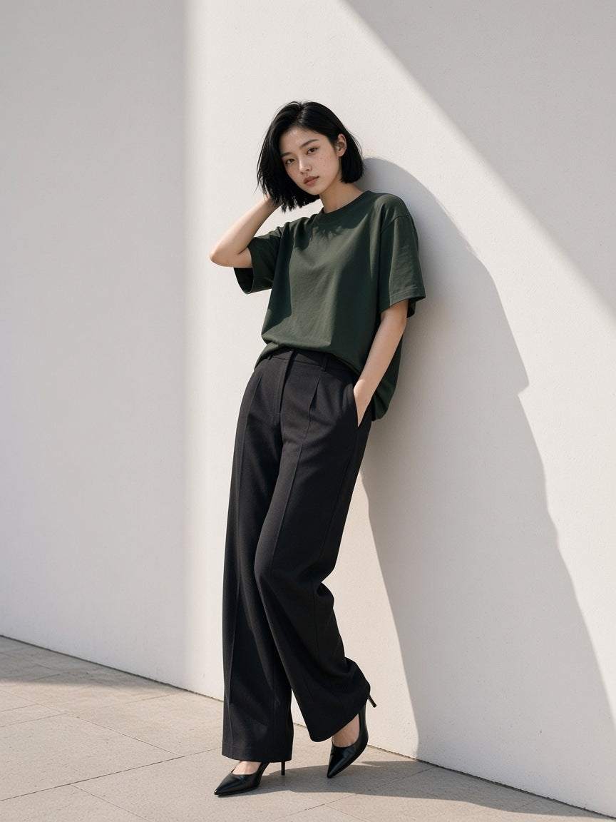 Woman in the Women's Heavyweight Boxy T-Shirt in Blackish Green with black wide trousers and heels, leaning on a white gallery wall in Hannam-dong, Seoul by day