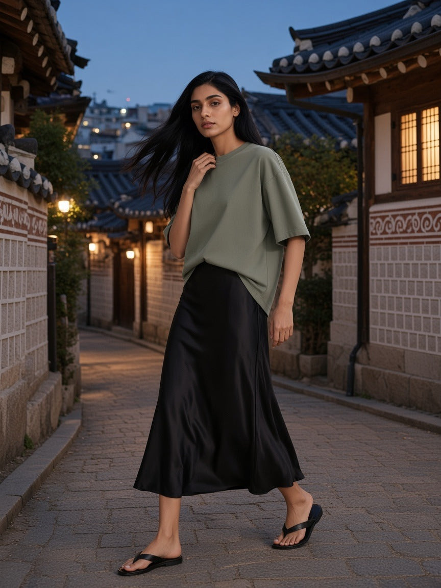 Woman in the Women's Heavyweight Drop Shoulder T-Shirt in Grey Green with a black satin midi skirt and flat sandals, turning in a hanok alley in Bukchon, Seoul at blue hour