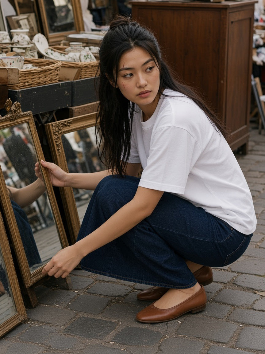Woman in the Women's Heavyweight Mineral Wash Boxy T-Shirt in White with a denim maxi skirt and ballet flats, browsing mirrors at a Paris flea market