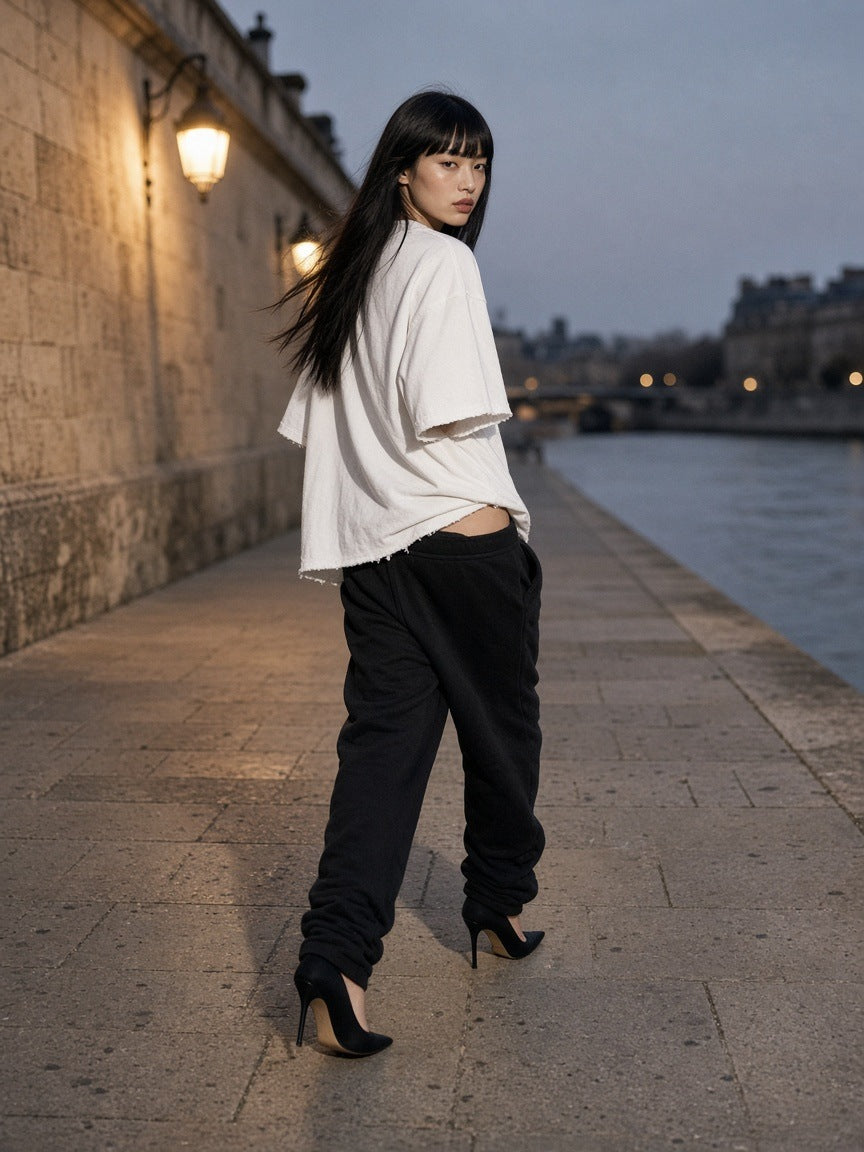 Woman in the Women's Heavyweight Vintage Washed Frayed T-Shirt in White on a limestone quai in Paris at blue hour