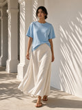 Woman in the Women's Oversized T-Shirt in Sky Blue under a palm-shaded plaster colonnade at a resort at golden hour