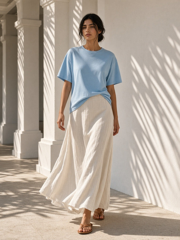 Woman in the Women's Oversized T-Shirt in Sky Blue under a palm-shaded plaster colonnade at a resort at golden hour