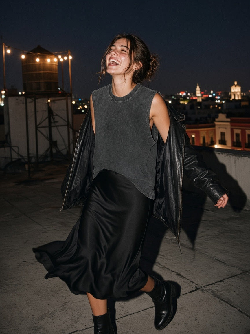 Woman in the Women's Snow Washed Frayed Hem Tank Top in Dark Gray with a black satin skirt and leather jacket, twirling on a Roma Norte rooftop in Mexico City at 2am