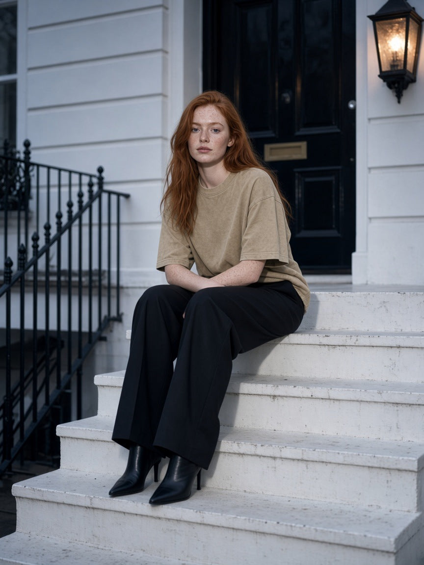 Woman in the Women's Snow Washed Heavyweight Oversize T-Shirt in Khaki on white stucco steps in London at blue hour