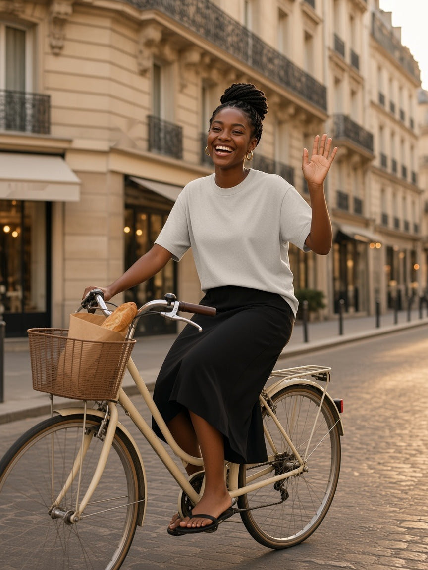 Woman in the Women's Heavyweight Drop Shoulder T-Shirt in Oat Gray cycling down a cobbled Paris street in the evening
