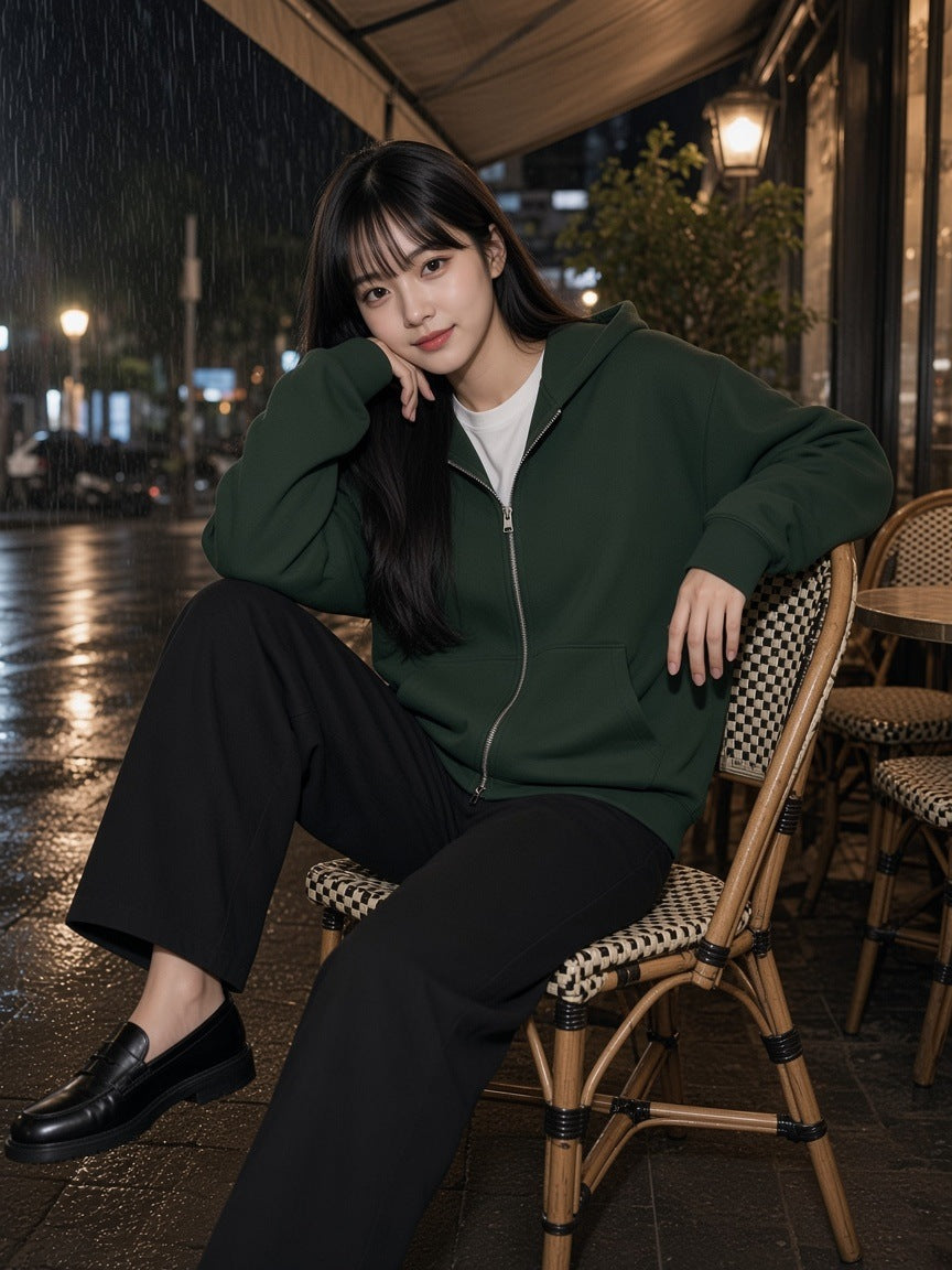 Woman in the Women's Heavyweight Full Zip Hoodie in Blackish Green on a Paris café terrace in the rain at night