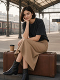 Woman in the Women's Heavyweight Mineral Wash Boxy T-Shirt in Black on a vintage suitcase under a Paris station canopy