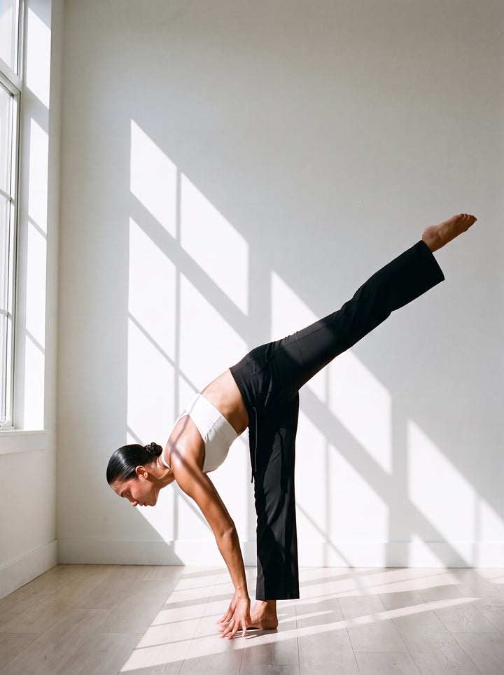 Woman in the Women's High Rise Straight Leg Yoga Pants in Black, in a standing split in a sunlit movement studio