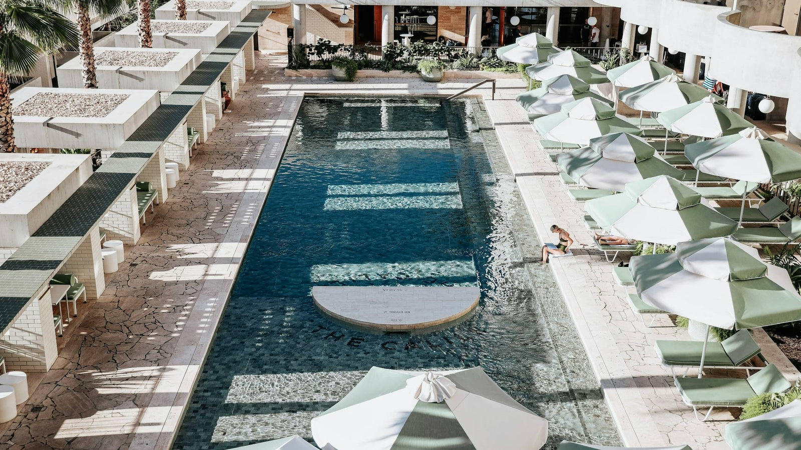 A hotel pool seen from above, white parasols along the water.