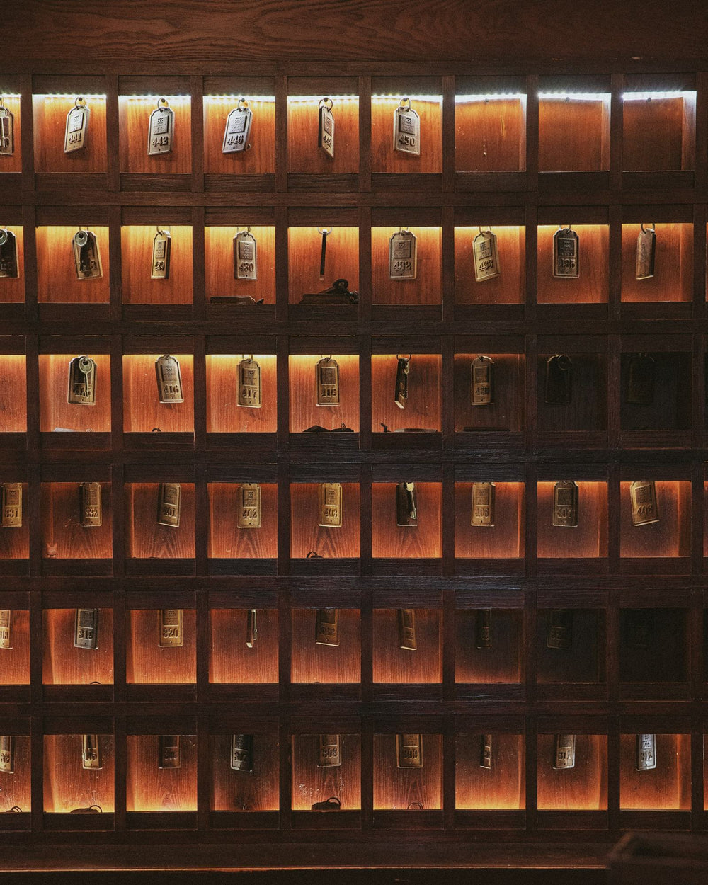 A wall of hotel room keys in lit wooden cubbies.